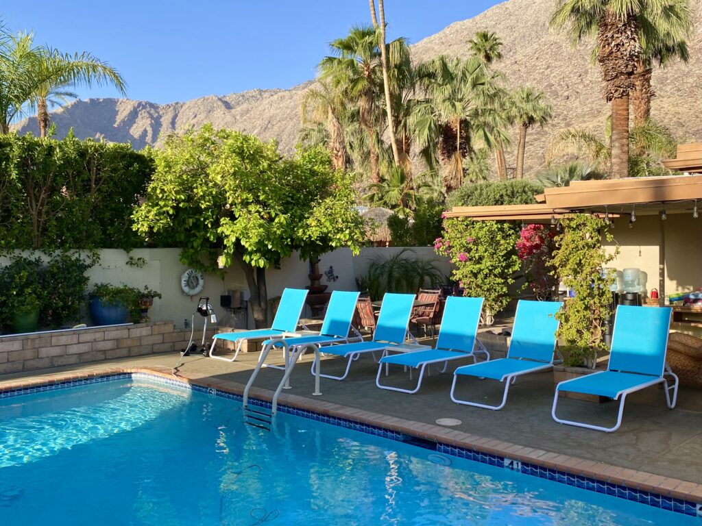 the pool featuring lounge chairs, great landscaping, palm trees, mountains and blue skies.